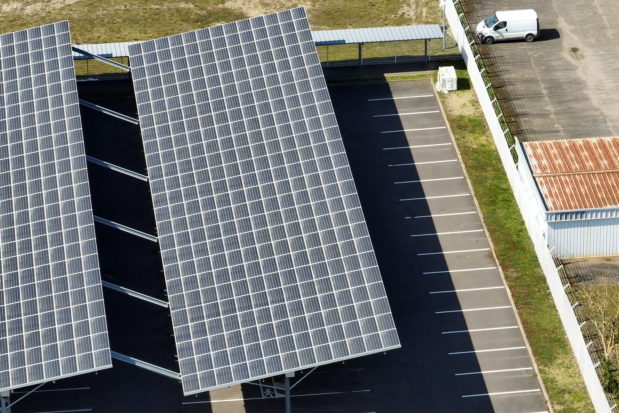 Aerial view of solar panels installed over parking lot with parked cars for effective generation of